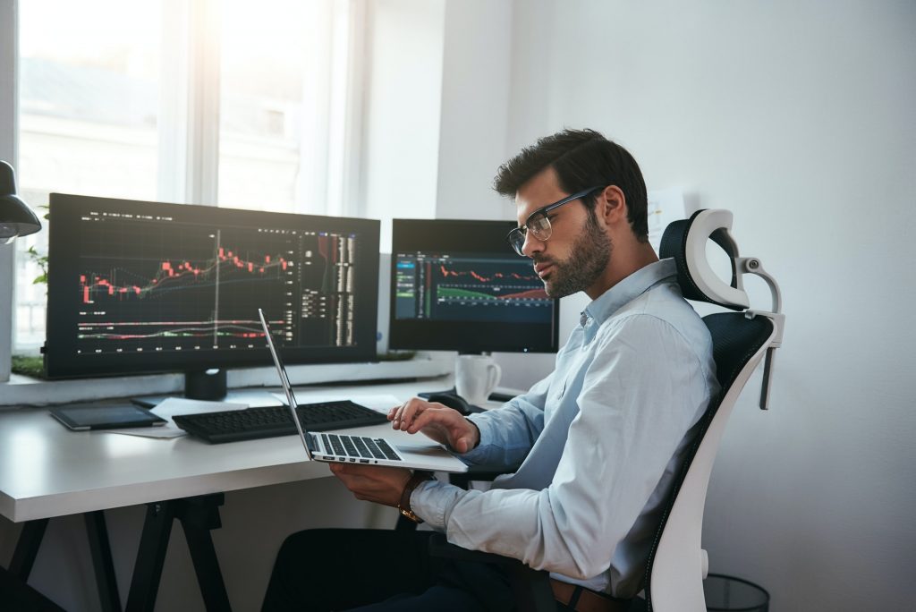 Bearded trader wearing eyeglasses analyzing financial market via laptop